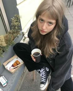 a girl holding a coffee cup and looking at the camera