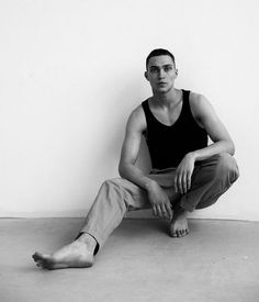 a man sitting on the floor in front of a white wall with his feet crossed