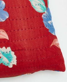 a red pillow with blue and pink flowers on the front, sitting on a white surface