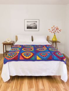 a bed with a colorful blanket on top of it in a bedroom next to a table