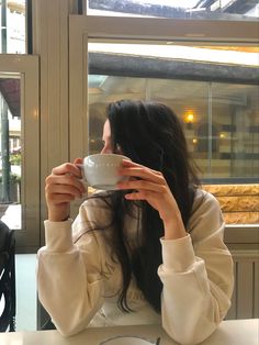 a woman sitting at a table drinking from a cup