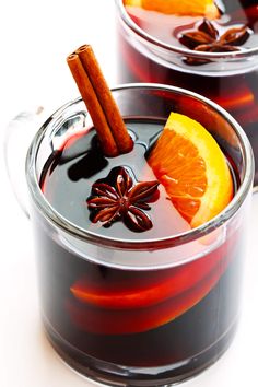 two glasses filled with red liquid and orange slices on top of each other, next to cinnamon sticks