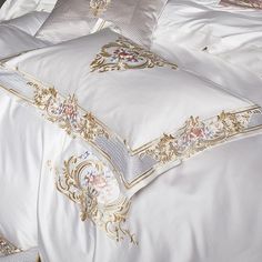 a white bed with gold trimmings and pillows on it's sides,