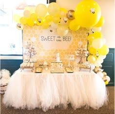 the dessert table is set up with yellow balloons and white tulle skirted tables