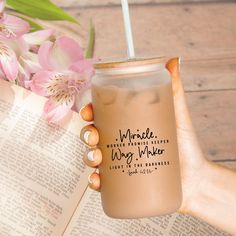 a person holding a drink in front of an open book with flowers on the table