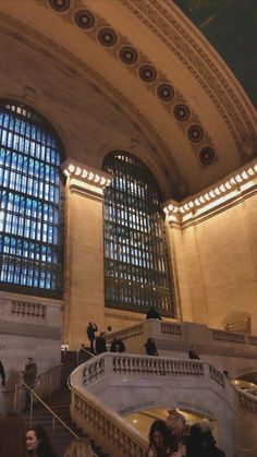 people are walking up and down the stairs in an ornate building with large windows on both sides