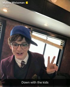 a young boy wearing glasses and a hat making the peace sign with his fingers in front of him