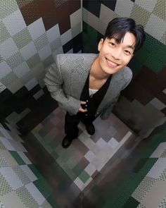 a man in a suit and tie standing in front of a wall with geometric tiles