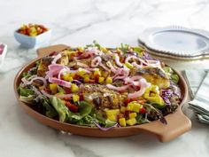 a salad in a pan on a table with other plates and utensils around it