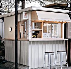 a small white building with two stools in front of it and an awning over the counter