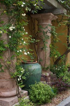 a green vase sitting on the side of a road next to trees and bushes in front of a building