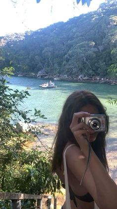 a woman taking a photo in front of a body of water with a camera on her shoulder