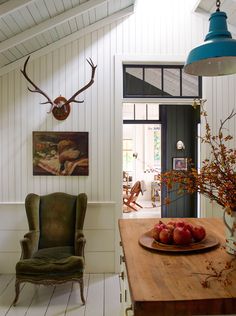 a wooden table topped with apples next to a vase filled with flowers and antlers