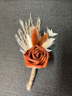 a boutonniere with feathers and an orange rose on the top is laying on a gray surface