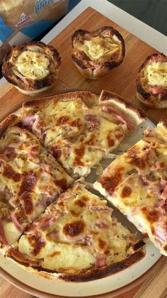 a pizza sitting on top of a wooden cutting board next to mini pies and bag of chips