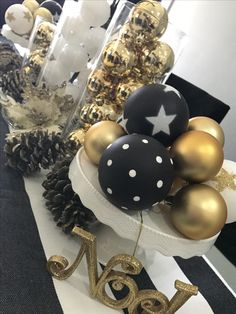 a table topped with lots of gold and black ornaments next to pineconi cones