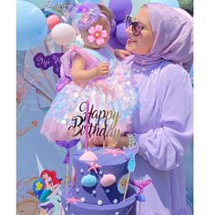 a woman holding a baby in her arms next to a birthday cake with mermaid decorations