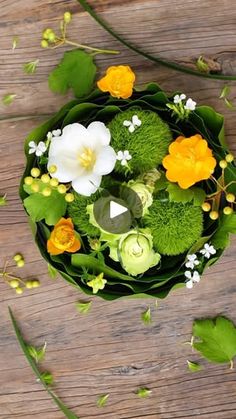 an arrangement of flowers arranged on a wooden table with green leaves and other greenery