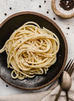 a black bowl filled with pasta on top of a table next to two spoons