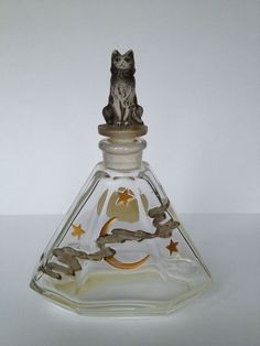 a glass bottle with a cat sitting on it's top and stars around the bottom