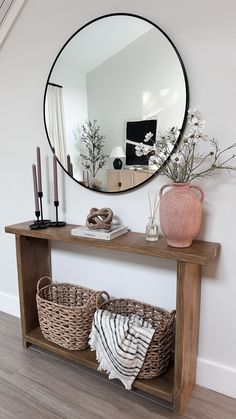 a mirror is hanging on the wall above a wooden shelf with baskets, candles and flowers