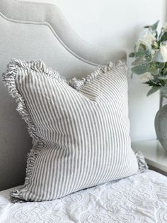 a white and gray striped pillow sitting on top of a bed next to a vase with flowers