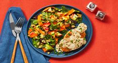 a blue plate topped with meat and salad next to two silver utensils on top of a red table