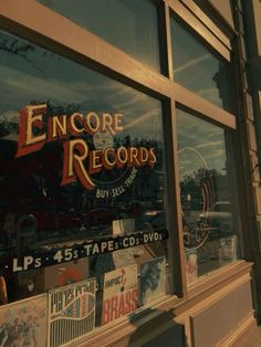 a store front window with various records on it's glass and the reflection of another building in the window