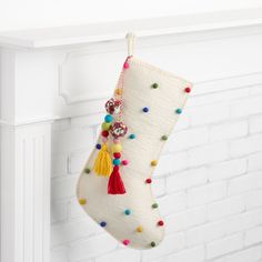 a white christmas stocking hanging from a mantel with tassels and beads