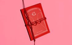 a red book tied to a string on a pink background