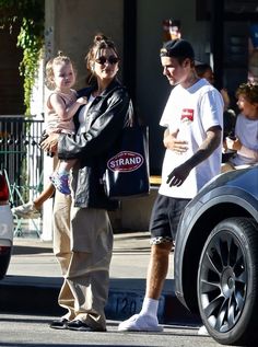 a man and woman walking down the street with a child in their arms, holding onto a bag