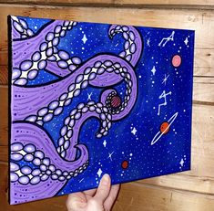 an octopus painting is being held up in front of a wooden wall with space and stars