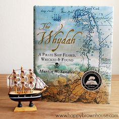 a book sitting on top of a wooden table next to a toy sailboat in front of it