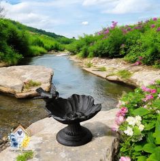 a statue sitting on top of a large rock next to a river filled with flowers