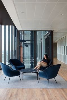 a woman sitting on a chair in a room with wooden floors and large glass windows