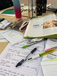 an open book sitting on top of a wooden table covered in papers and writing utensils