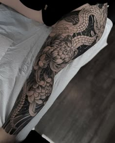 a woman's arm with a dragon tattoo on it and flowers in the background