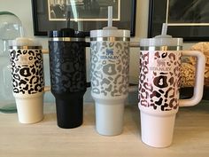 four travel mugs are lined up on a counter top in front of a framed photograph