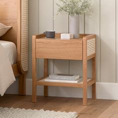 a small wooden table with a plant and books on it next to a white bed