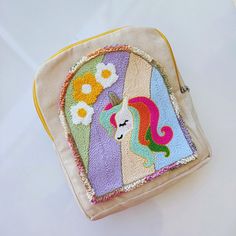 an embroidered purse with a unicorn on the front and flowers on the back, sitting on a white surface