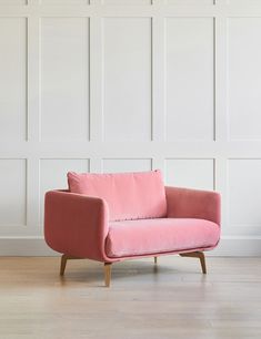 a pink chair sitting on top of a hard wood floor next to a white wall