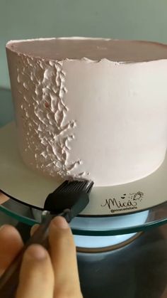 someone is decorating a white cake with pink frosting and a black plastic fork