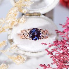 a blue ring sitting on top of a white box next to some pink and gold flowers