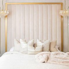 a white bed topped with lots of pillows next to two chandeliers and lamps