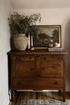 a wooden dresser with a potted plant on top of it next to a painting