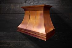 a copper range hood against a wooden wall