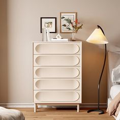 a white dresser sitting in a bedroom next to a lamp and pictures on the wall