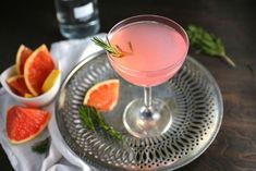 a drink in a glass on a silver tray with grapefruit and orange slices