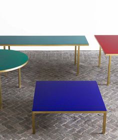 three tables with different colored tops sitting on a brick floor