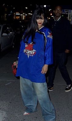 a woman in blue jacket and jeans walking down the street with her hand on her hip